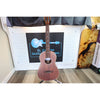 A Kala KA-SA-B All-Solid Acacia Baritone Ukulele with a reddish-brown body and dark neck stands on a stand in front of ECG Music.