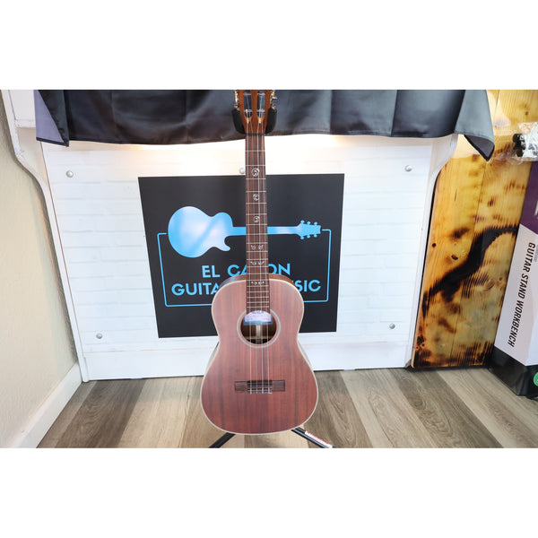 A Kala KA-SA-B All-Solid Acacia Baritone Ukulele with a reddish-brown body and dark neck stands on a stand in front of ECG Music.