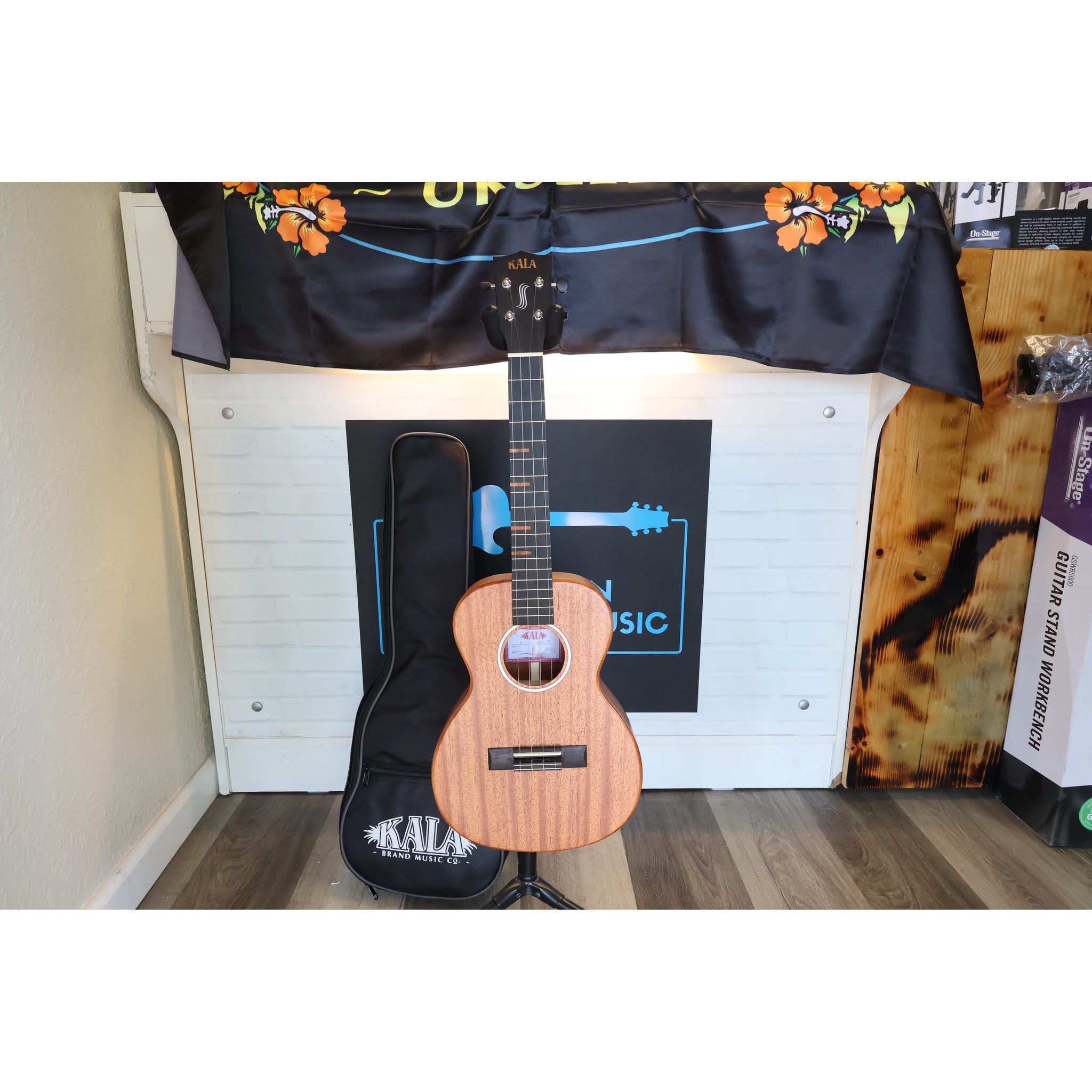 A Kala KA-WF-AMHG-T All Solid Mahogany Waterfall Tenor Ukulele at ECGMusic.with a natural wood finish stands on a stand in front ECG Music.
