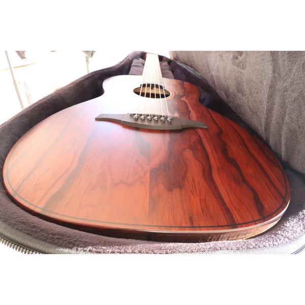 The Lâg Sauvage PE Parlor Acoustic-Electric Guitar in the hybrid case it comes with, providing great padding and protection.  The bronco wood grain  on the top is stunning, and you can see the edge of the rough cut side wood.