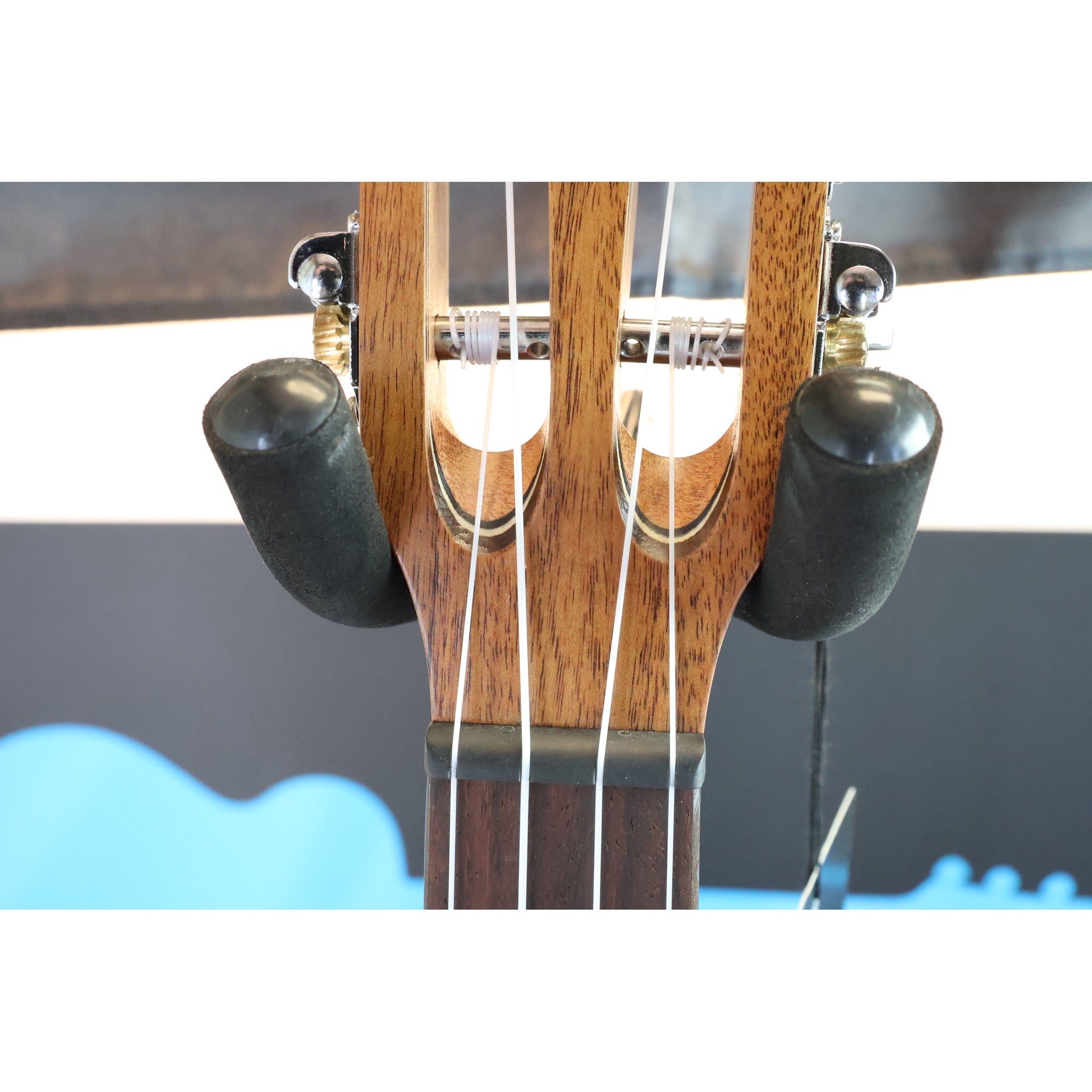 Close-up of a A Kala KA-SA-TE-C All-Solid Acacia Tenor Cutaway Ukulele with Fishman Electronics ukulele  mounted in a black guitar stand, with tuning pegs and strings visible against the ECGMusic logo.