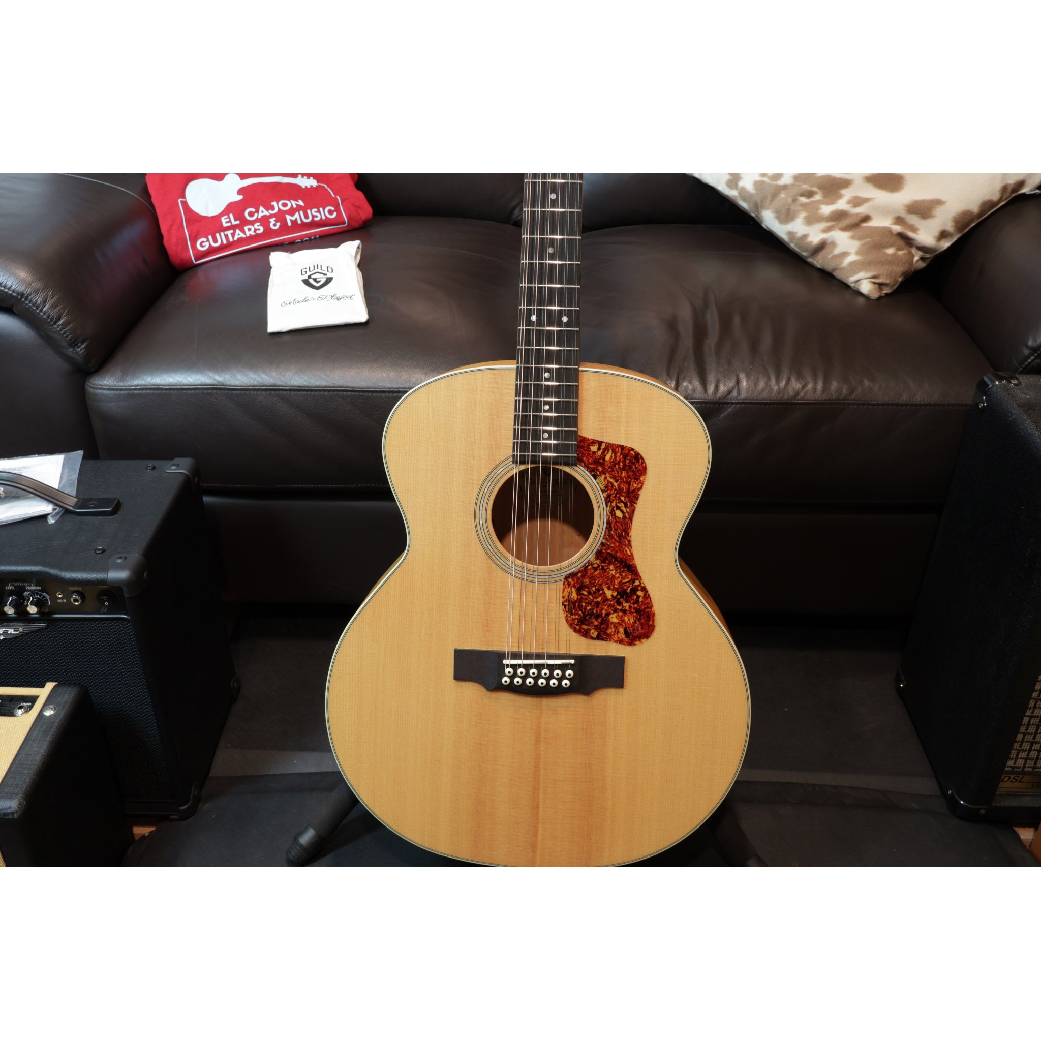 Acoustic guitar on a stand with a brown leather couch and guitar accessories in the background