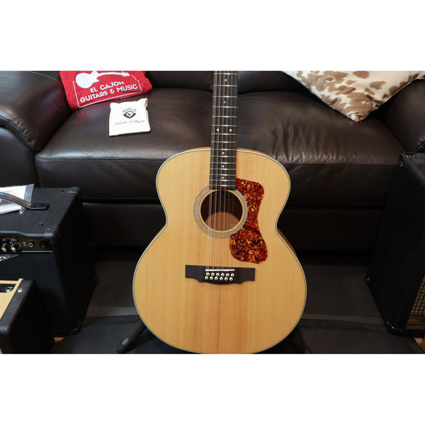 Acoustic guitar on a stand with a brown leather couch and guitar accessories in the background
