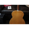 Back of a wooden acoustic guitar with a dark couch and a white pillow in the background.