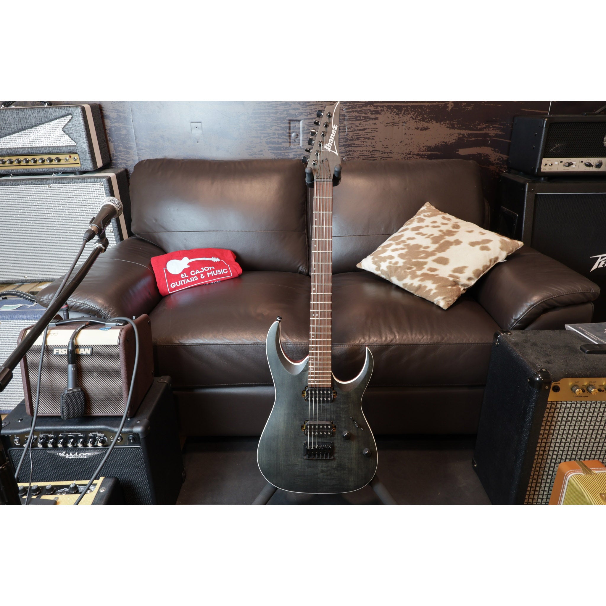 Electric guitar leaning against a brown leather couch with amplifiers on either side.