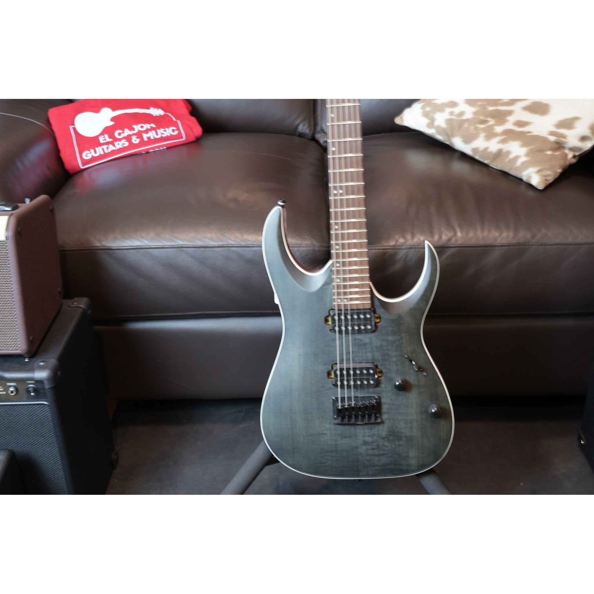 Electric guitar on a dark brown couch with a red box labeled 'El Cajon Guitar Music' in the background.