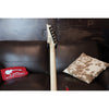 Guitar leaning against a brown couch with decorative pillows and a textured wall background