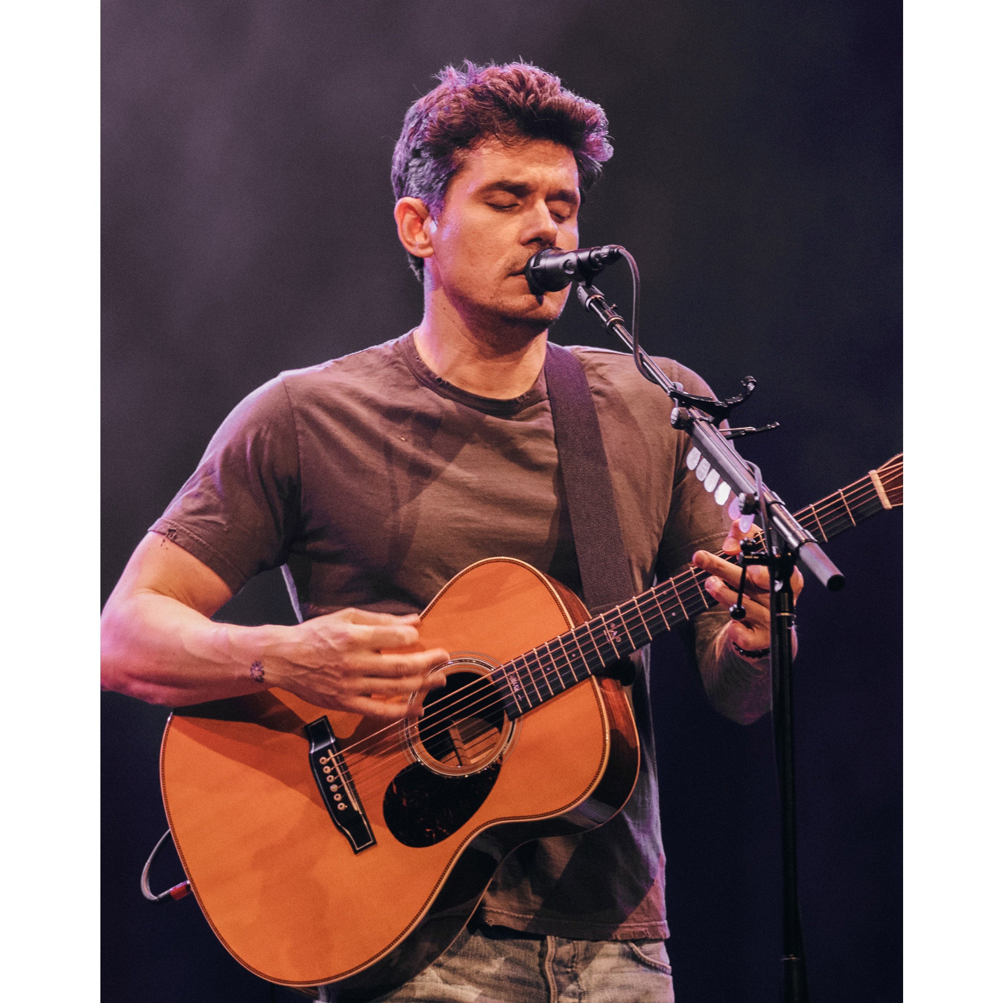 Man playing an acoustic guitar on stage with a microphone
