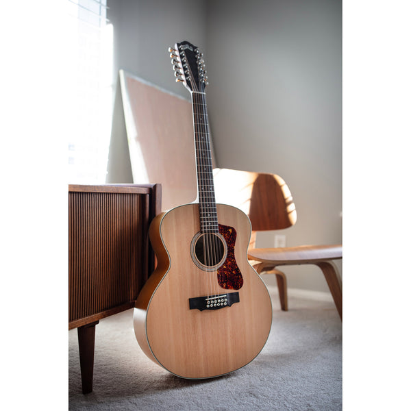 Acoustic guitar leaning against a wooden cabinet in a room with chairs and a window.