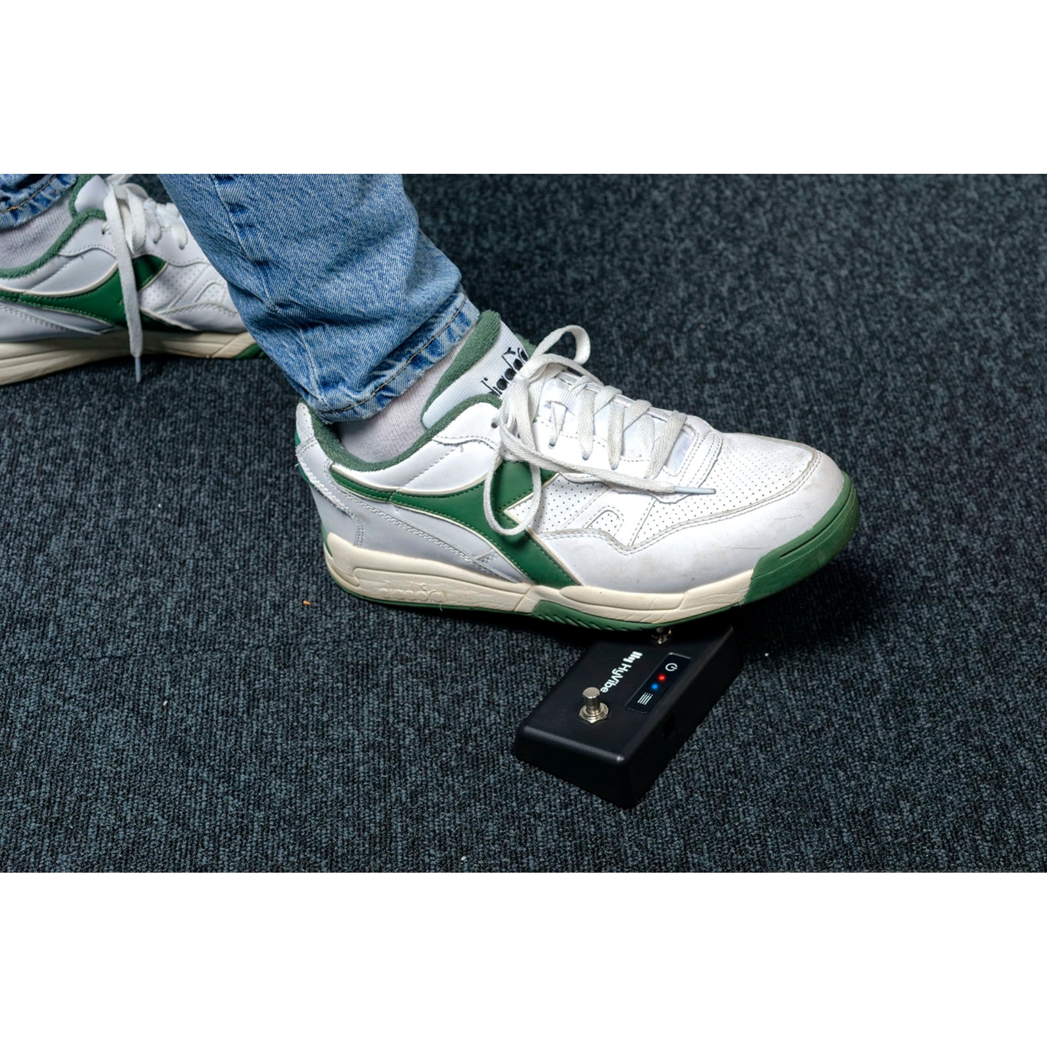 White and green sneakers on a dark textured surface with a small black device in front.