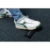 White and green sneakers on a dark textured surface with a small black device in front.