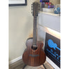12 string Acoustic Electric guitar leaning against a wall with a store sign in the background