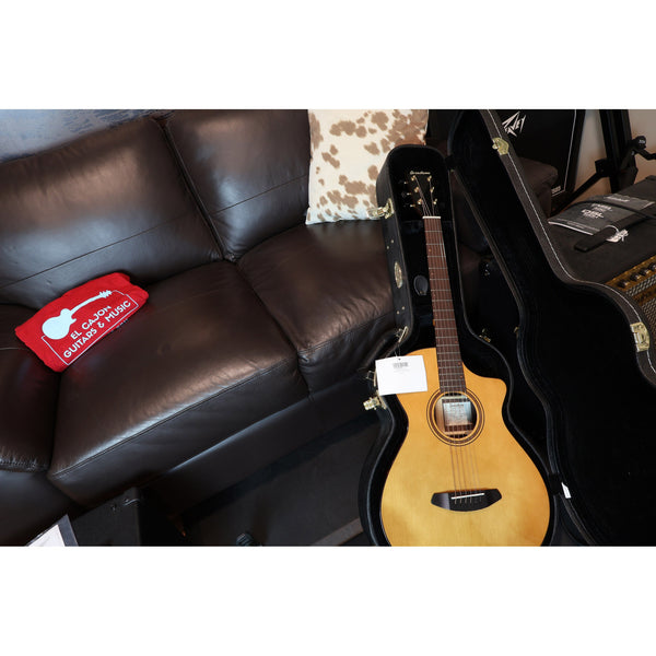 Acoustic guitar in a case next to a brown leather couch with a red sign.