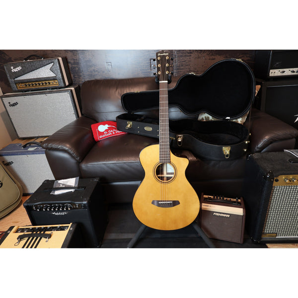 Acoustic guitar with case on a couch surrounded by amplifiers and equipment