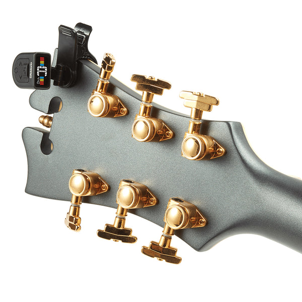 Close-up of a D'Angelico guitar headstock with six gold tuning pegs and a black digital tuner clipped to the upper left, shown on a white background.