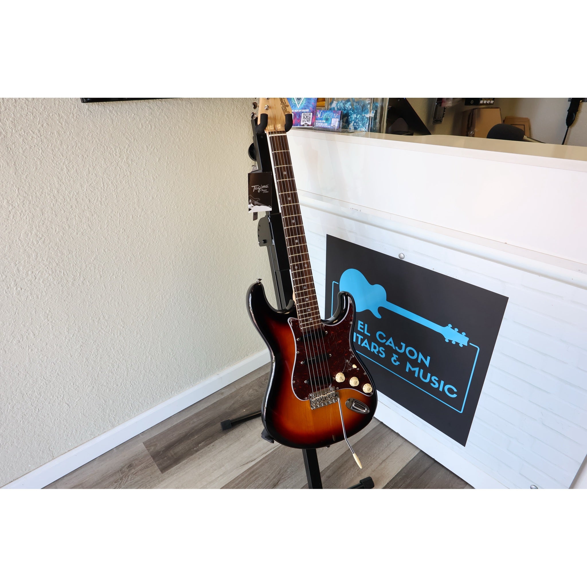 Electric guitar on a stand against a wall with a music store sign in the background