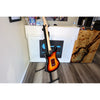 Electric guitar on a stand in a room with a white wall and wooden floor.