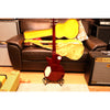 Guitar in a yellow case on a stand in front of a brown couch with an amplifier to the side.