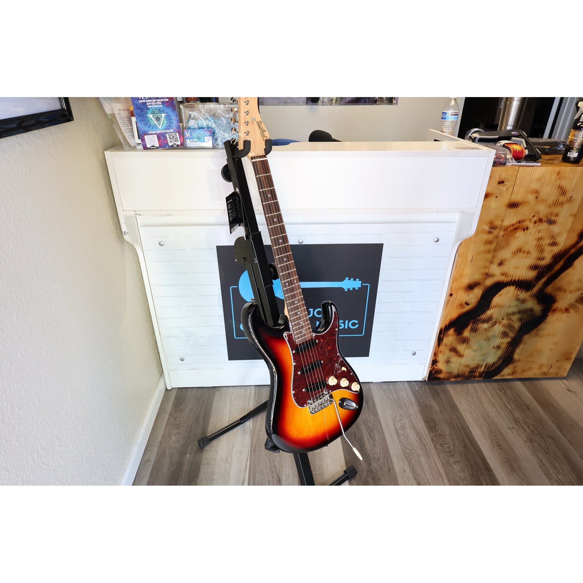 Electric guitar on a stand in a room with a visible brand logo on the wall.