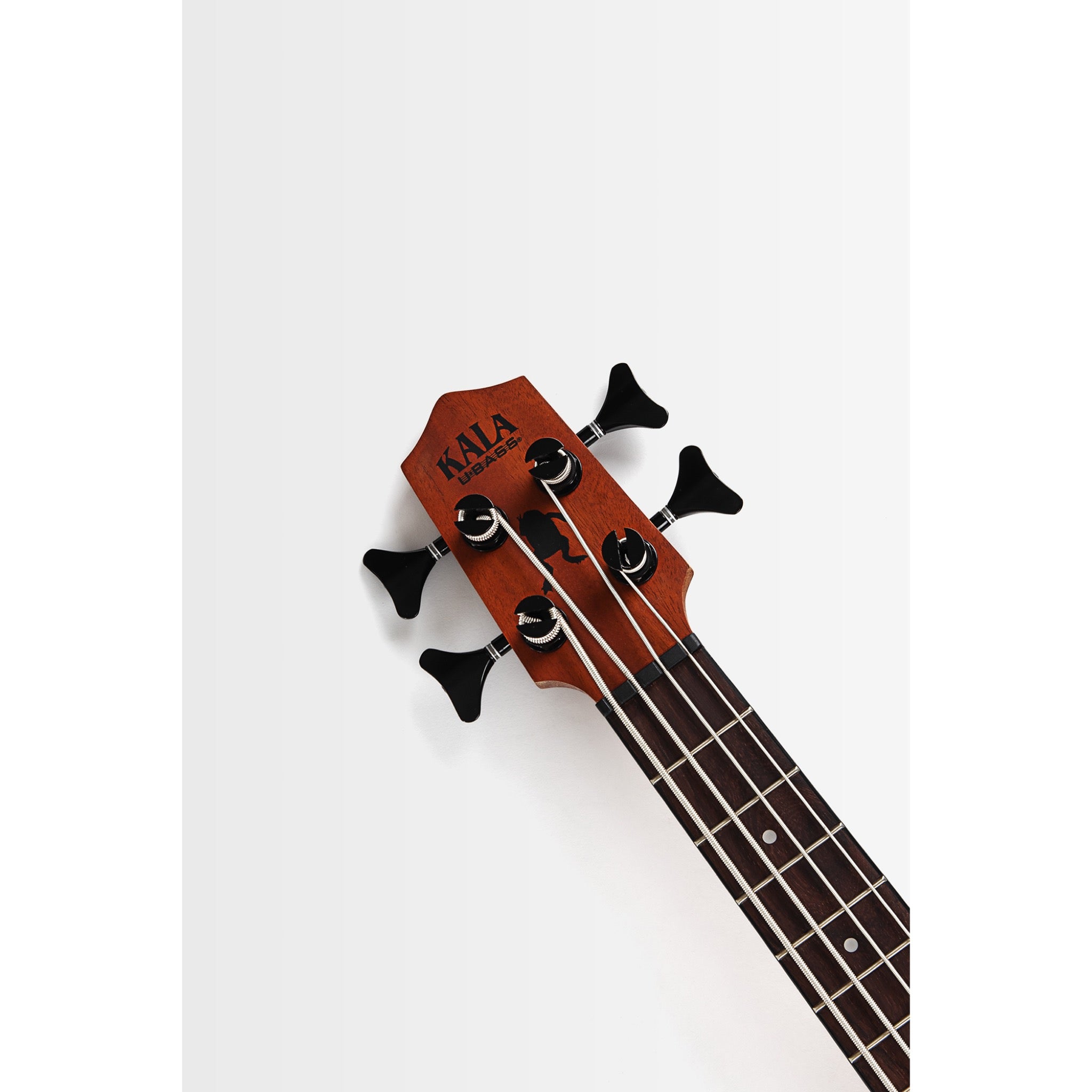 Close-up of the headstock of a Kala Nomad Acoustic-Electric U•BASS® - UBASS-NOMAD-FS, showing the brand name 'KALA' in black on a reddish-brown wood tone, with four black tuning keys and strings extending down the dark fretboard against a clean white background.