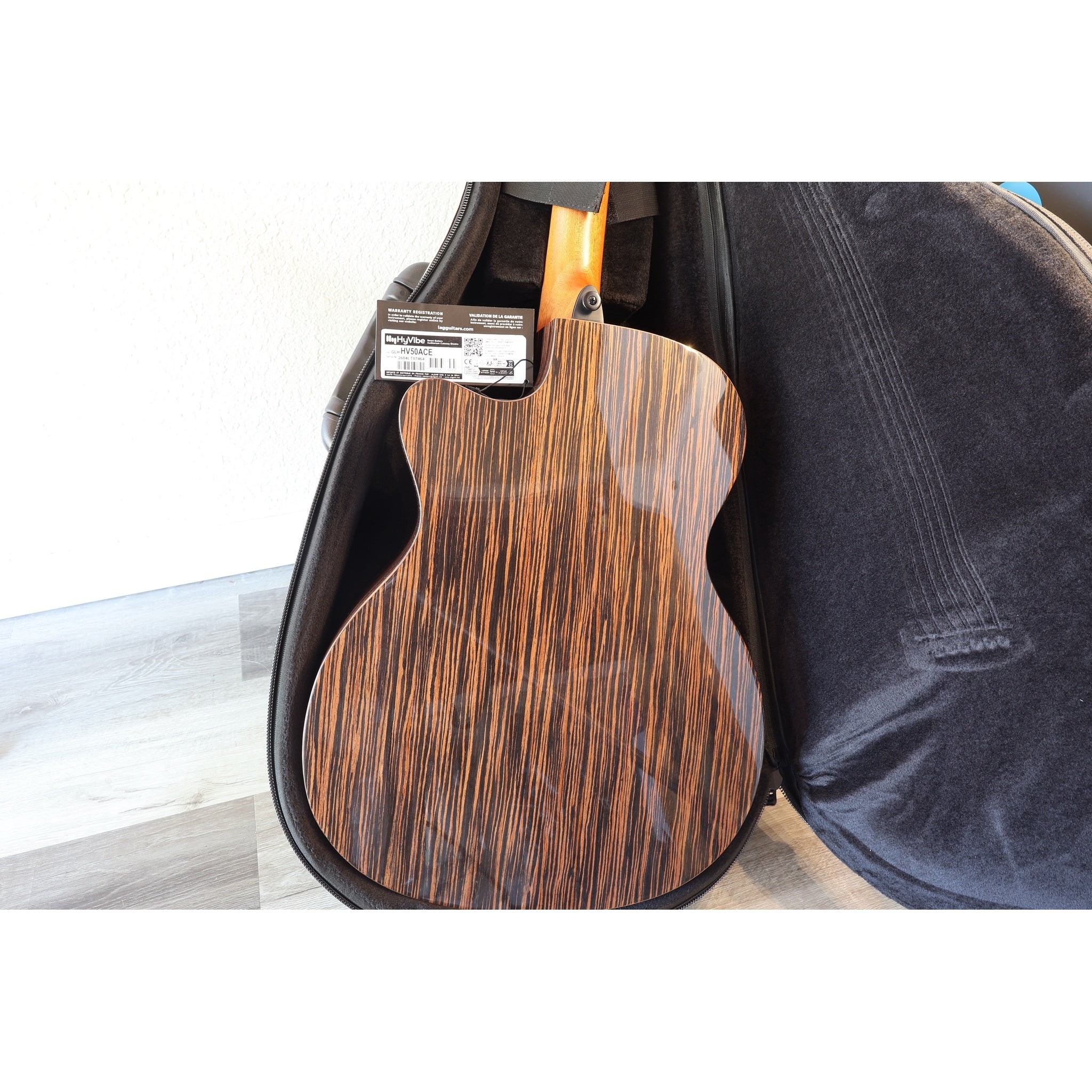 Lâg HyVibe 50 Auditorium Bevel Cutaway Smart Guitar – HV50ACE-2604LT07464 back in case with Lâg HyVibe 50 warranty card, serial number, upc showing.