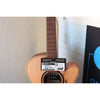 This Lâg HyVibe 10 HV10ACE with Warranty Registration Card showing Serial Number 2604LT07360 and UPC hung on the guitar at the strings on the neck at the body, with the soundhole and sticker showing beneath it.