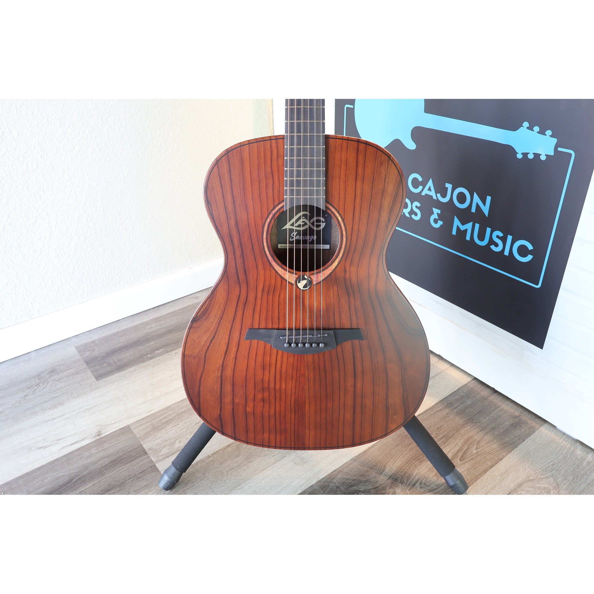 The guitar body cloesup in a stand at the front of El Cajon Guitars & Music with part of the front desk and logo showing.  This guitar is the Lâg Sauvage-A Auditorium Acoustic Guitar with Serial 2511LT20951.