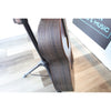 Close-up of the side and back of an acoustic guitar with a dark wood grain finish, resting on a black stand on a light wood floor.