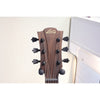Close-up of the headstock of an LG acoustic guitar, showing the dark brown wood grain, six black tuning pegs, and the gold LG logo, set against a light-colored wall.