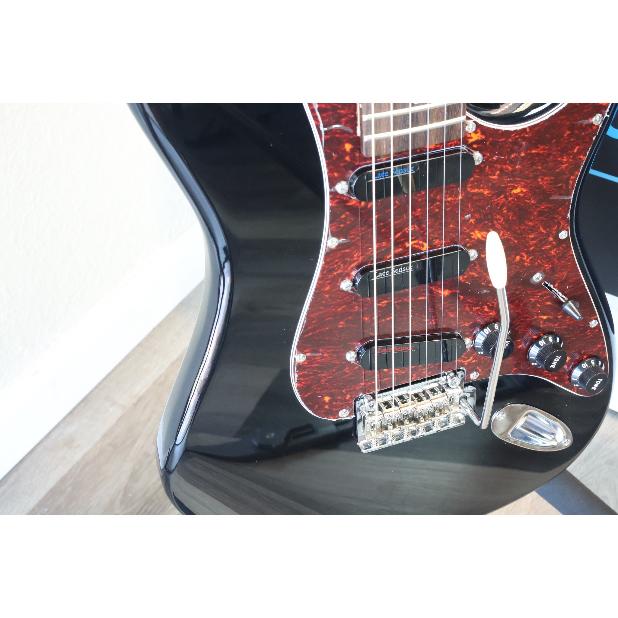 Closeup of the Tagima T-635 Classic Black Electric Guitar showing the Lace Sensor Red/Silver/Blue Pickups, the trem bar control knobs, selector switch, output jack., and pickguard.